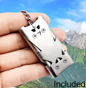 Photo of a hand holding a survival whistle, with a background of mountains.